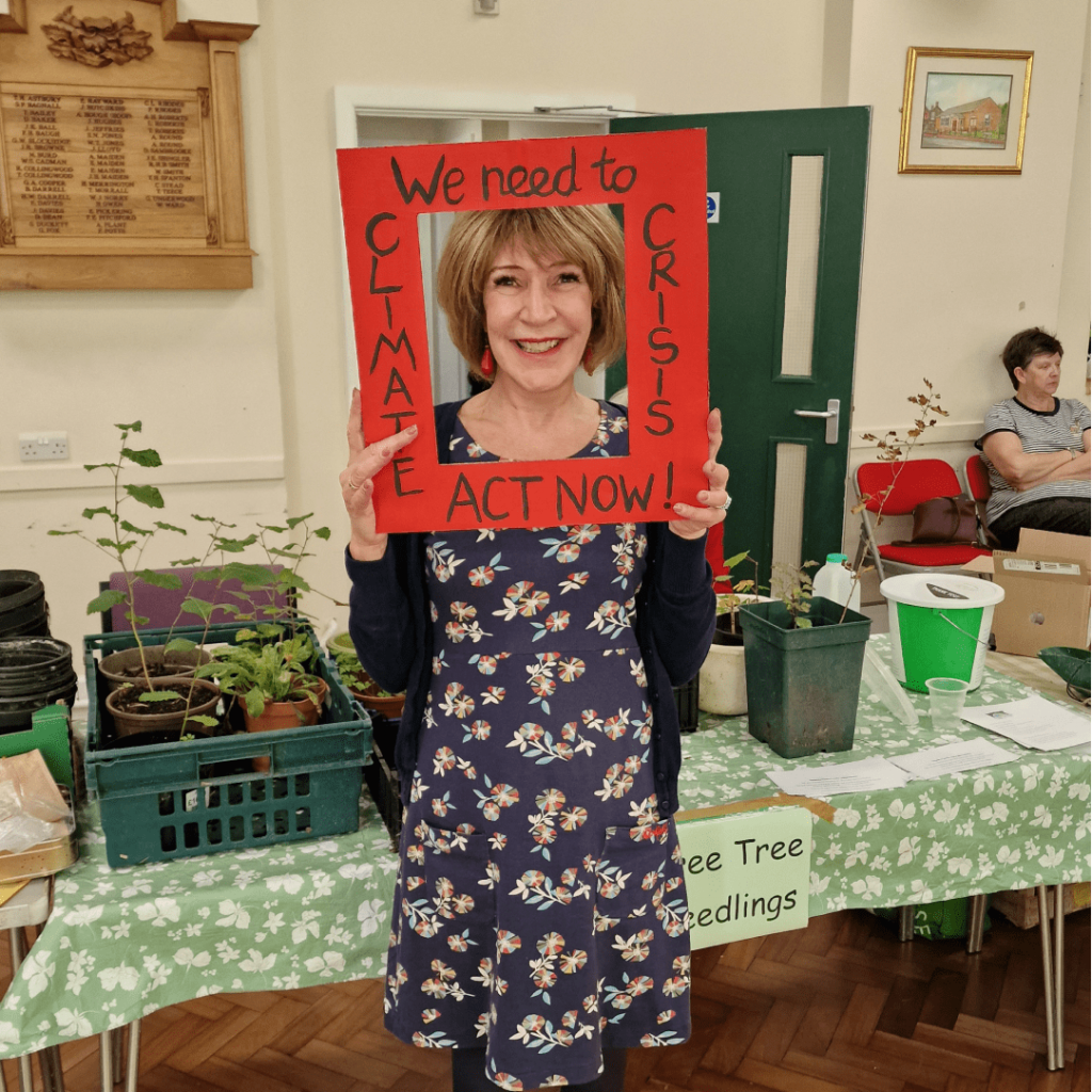 A smiling visitor at the Harvest Local holding a red, cardboard frame that says "Climate Crisis: I demand action now".